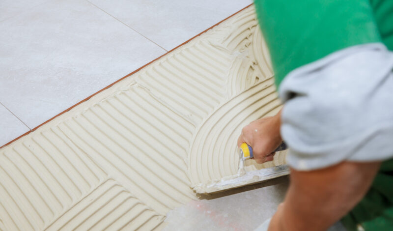 worker-installs-tiles-floor-he-put-glue-using-comb-trowel-master-puts-adhesive