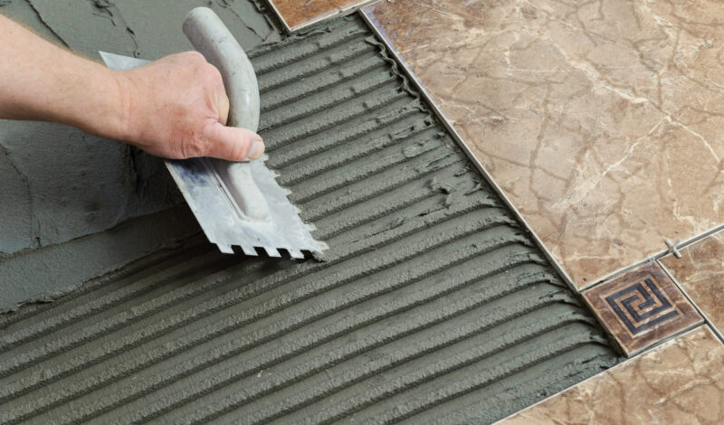 laying-ceramic-tiles-troweling-adhesive-onto-concrete-floor-preparation-laying-white-floor-tile